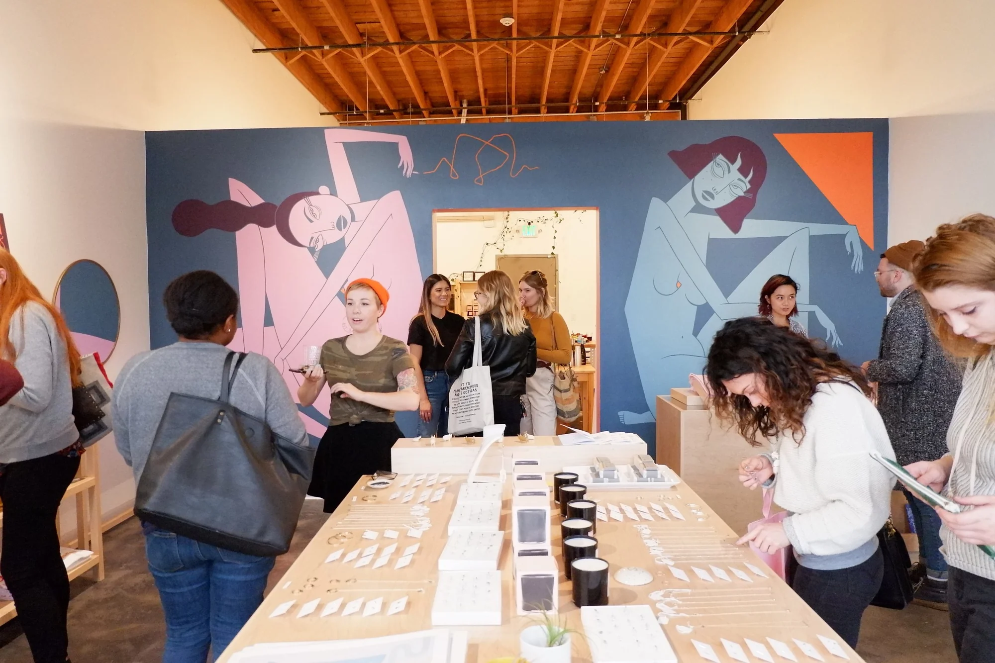 Visitors gathered around a jewelry table in front of the mural wall at a shop event.